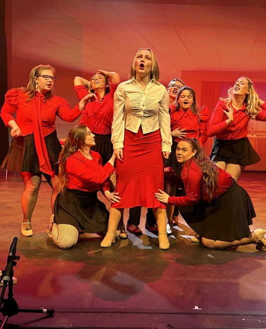 Energetic musical number featuring a group of performers dressed in red, singing passionately on stage. Energetic musical number featuring a group of performers dressed in red, singing passionately on stage.